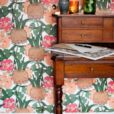 Wooden desk with drawers and art supplies against wallpaper n a handrawn details floral pattern in orange, red and green on a white field. 