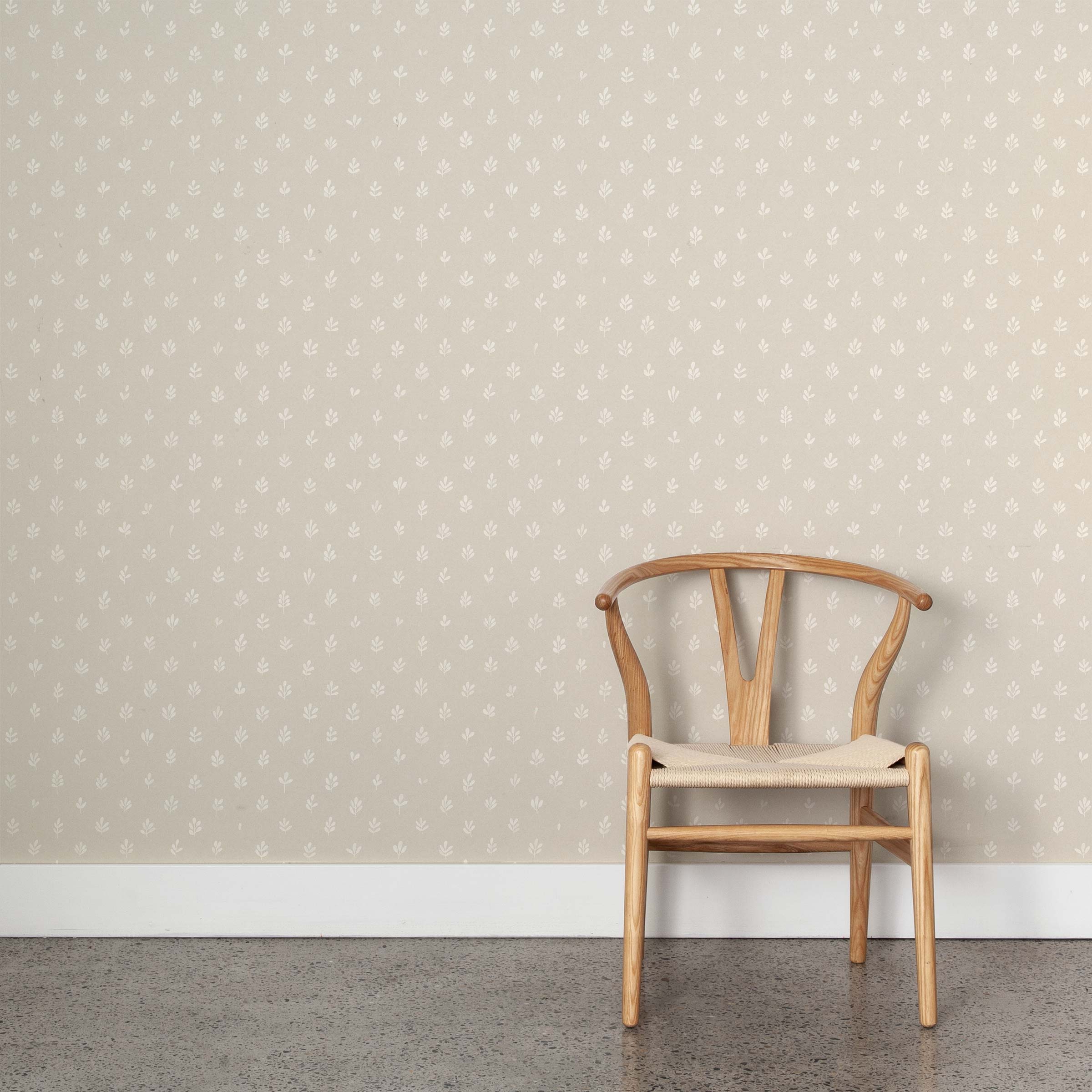A wooden chair stands in front of a wall papered in a repeating leaf print in white on a cream field.