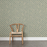 A wooden chair stands in front of a wall papered in a repeating leaf print in navy on a sage field.