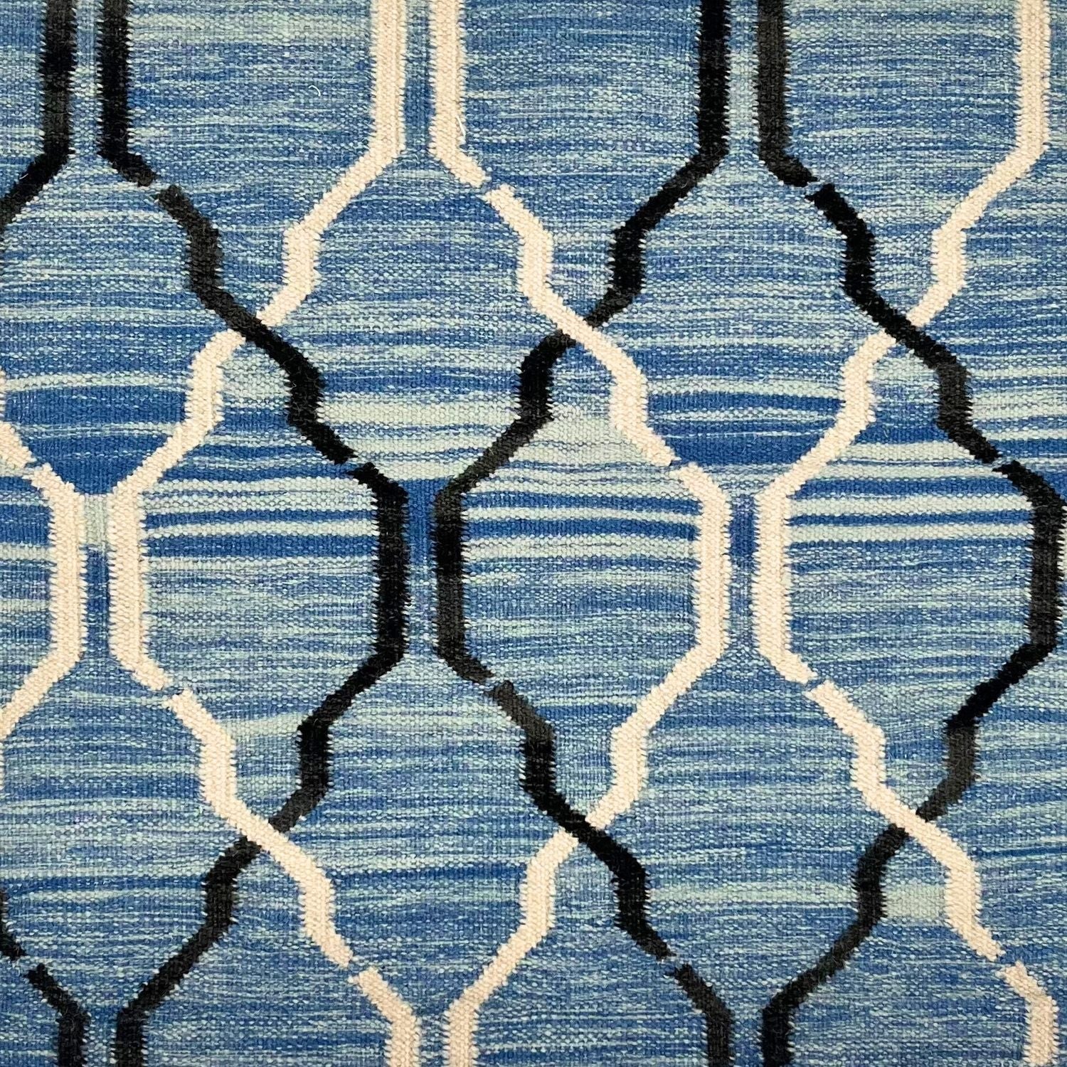 Detail of flatwoven rug with a black and white lattice design over a mottled blue ground