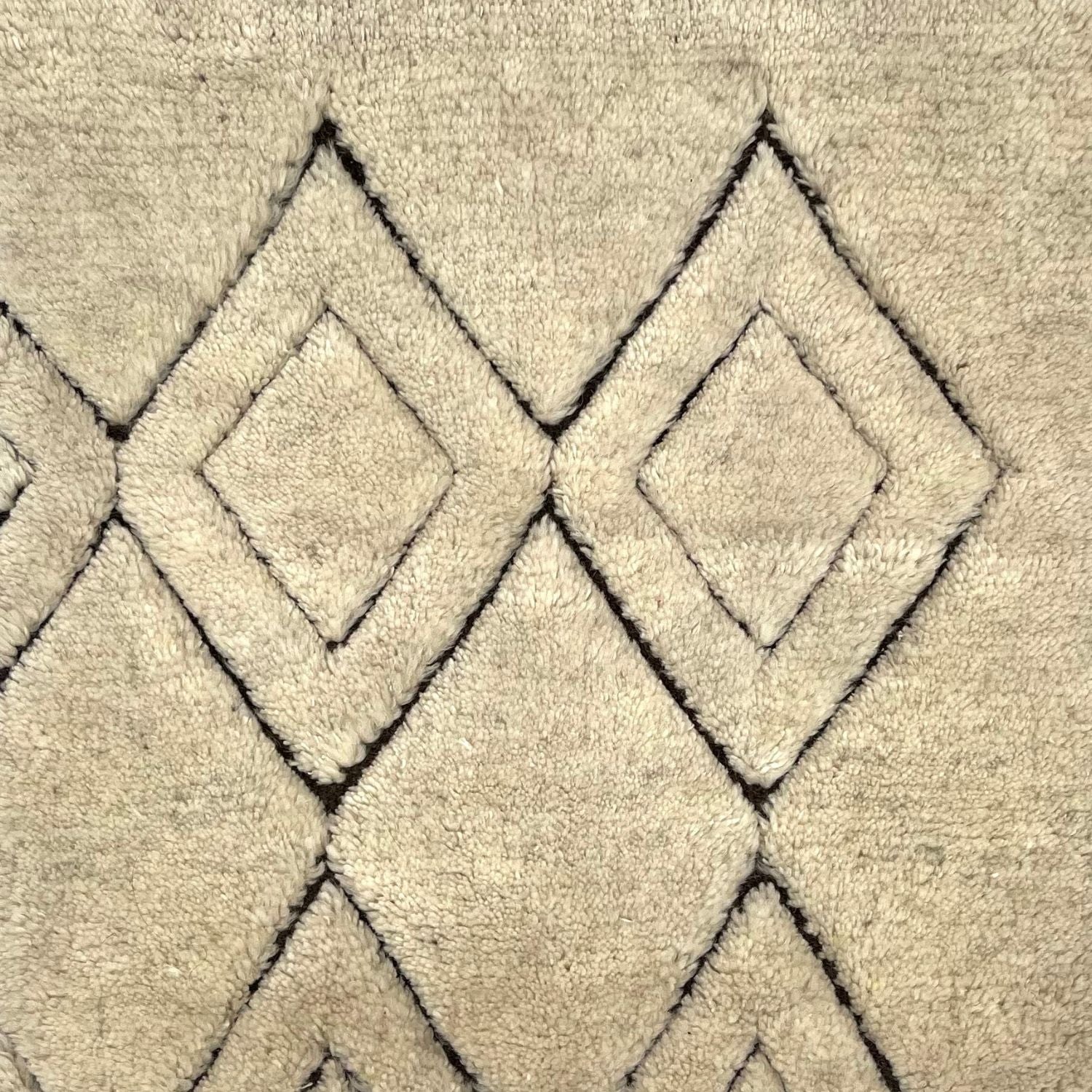 A beige rug with black diamond pattern across a natural raised plush ground.
