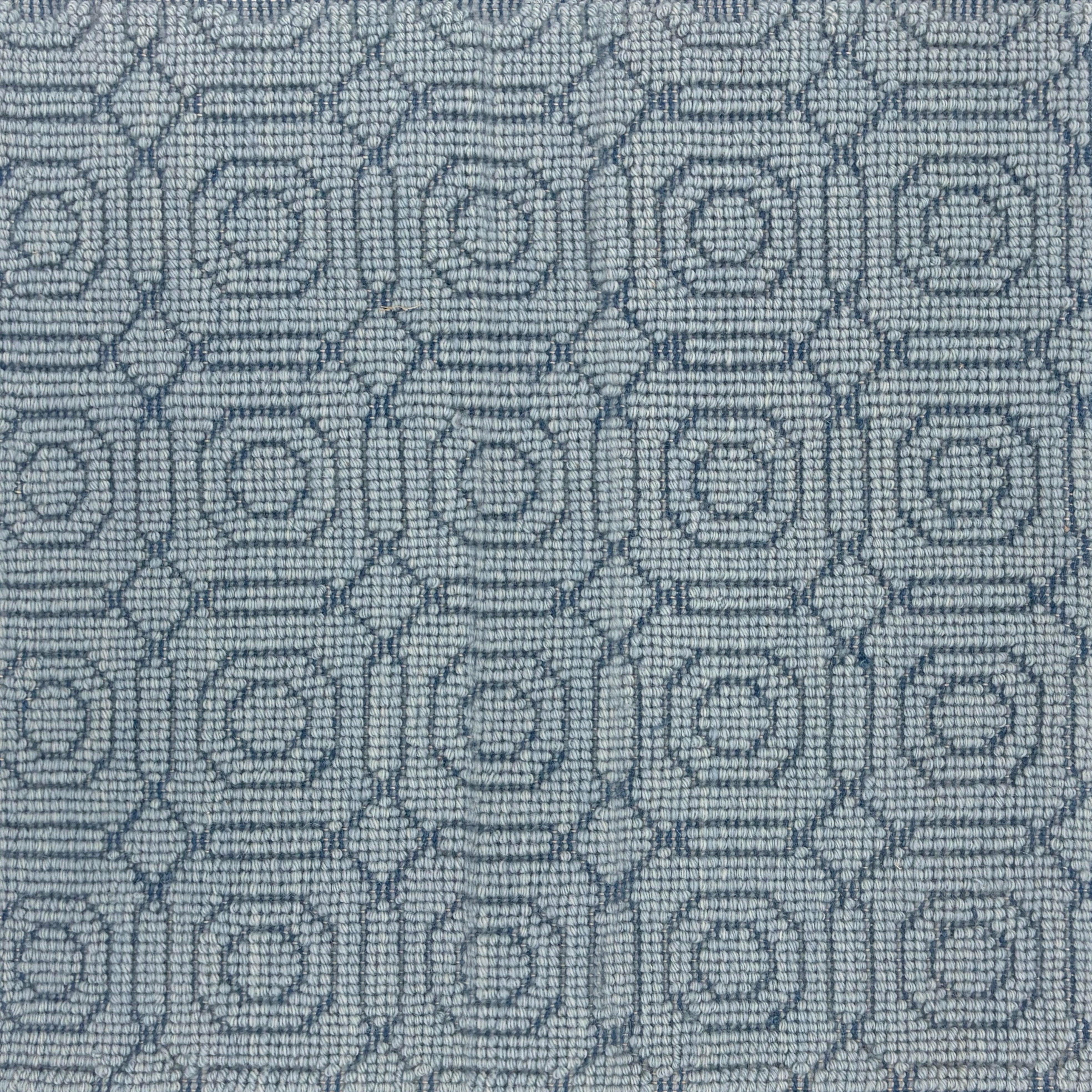 Handwoven rug sample with a raised loop circle and diamond pattern in shades of blue. 