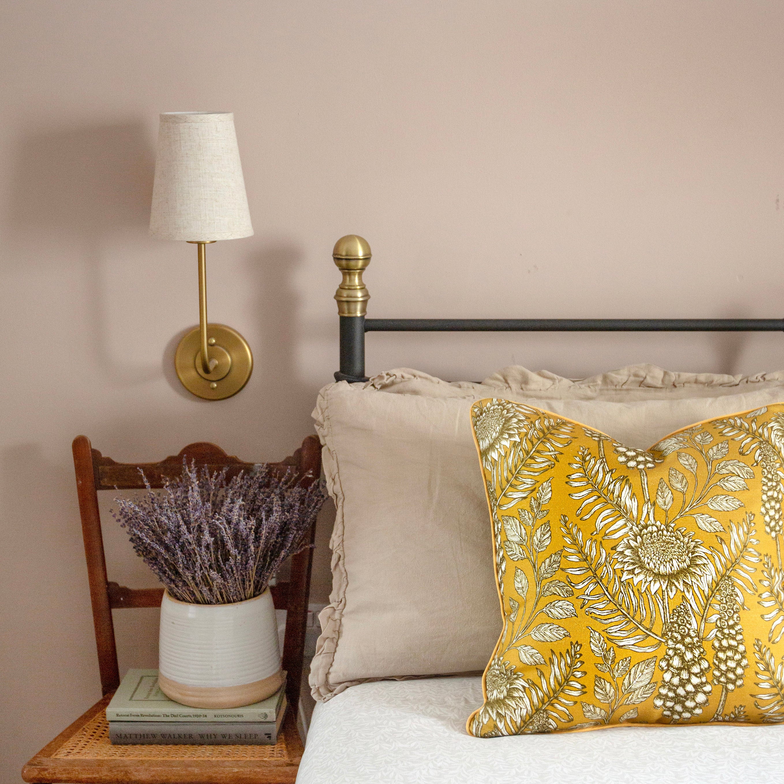 A cozy bedroom tableau with flowers, books and a large throw pillow upholstered in floral fabric in black, white and yellow.