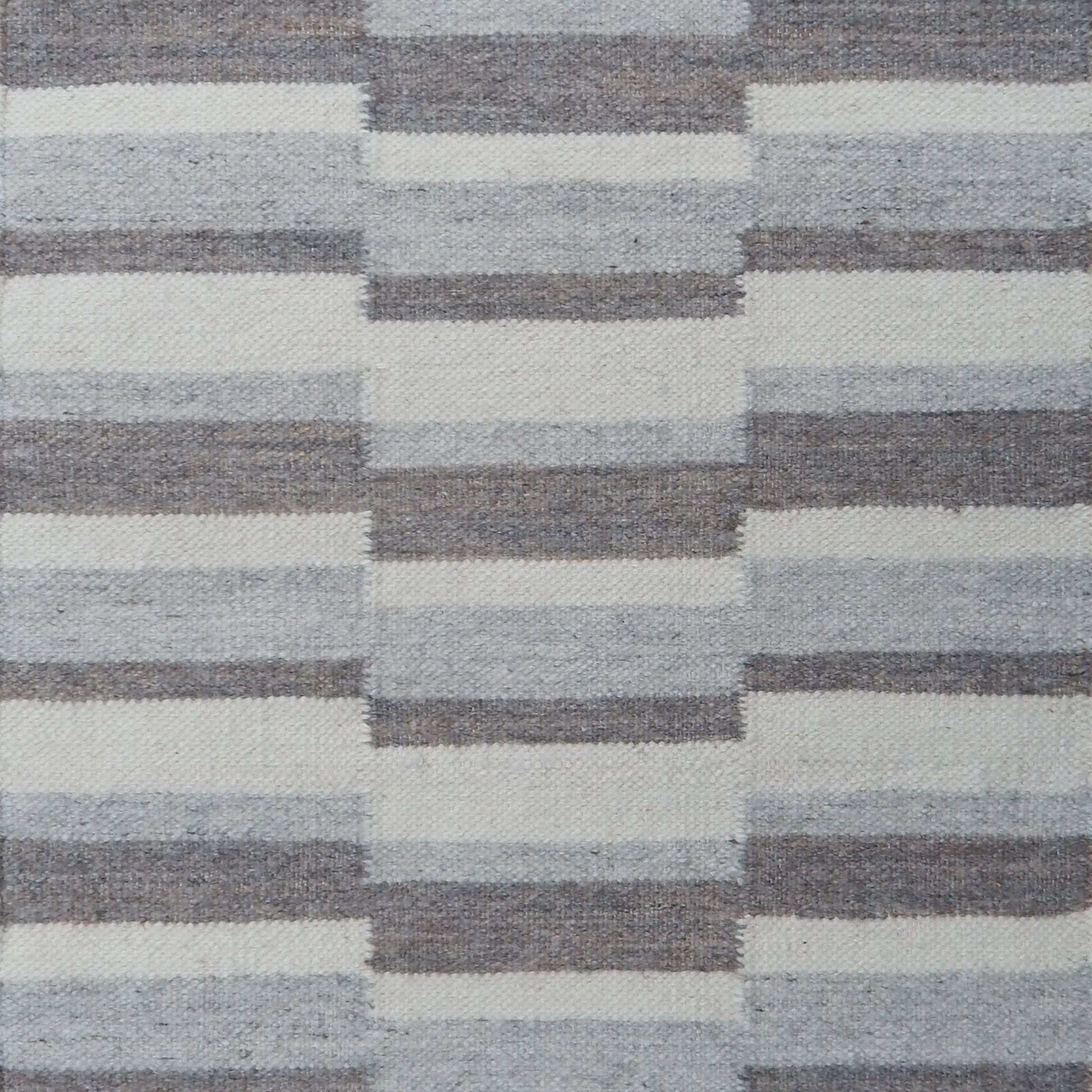 Flatweave rug in a broken stripe in shades of grey and cream.
