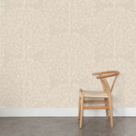 A wooden chair stands in front of a wall papered in a repeating owl and tree print in white on a cream field.