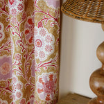 Curtain in printed linen in a handdrawn playful floral design in coral, lilac and red against a tan field. 