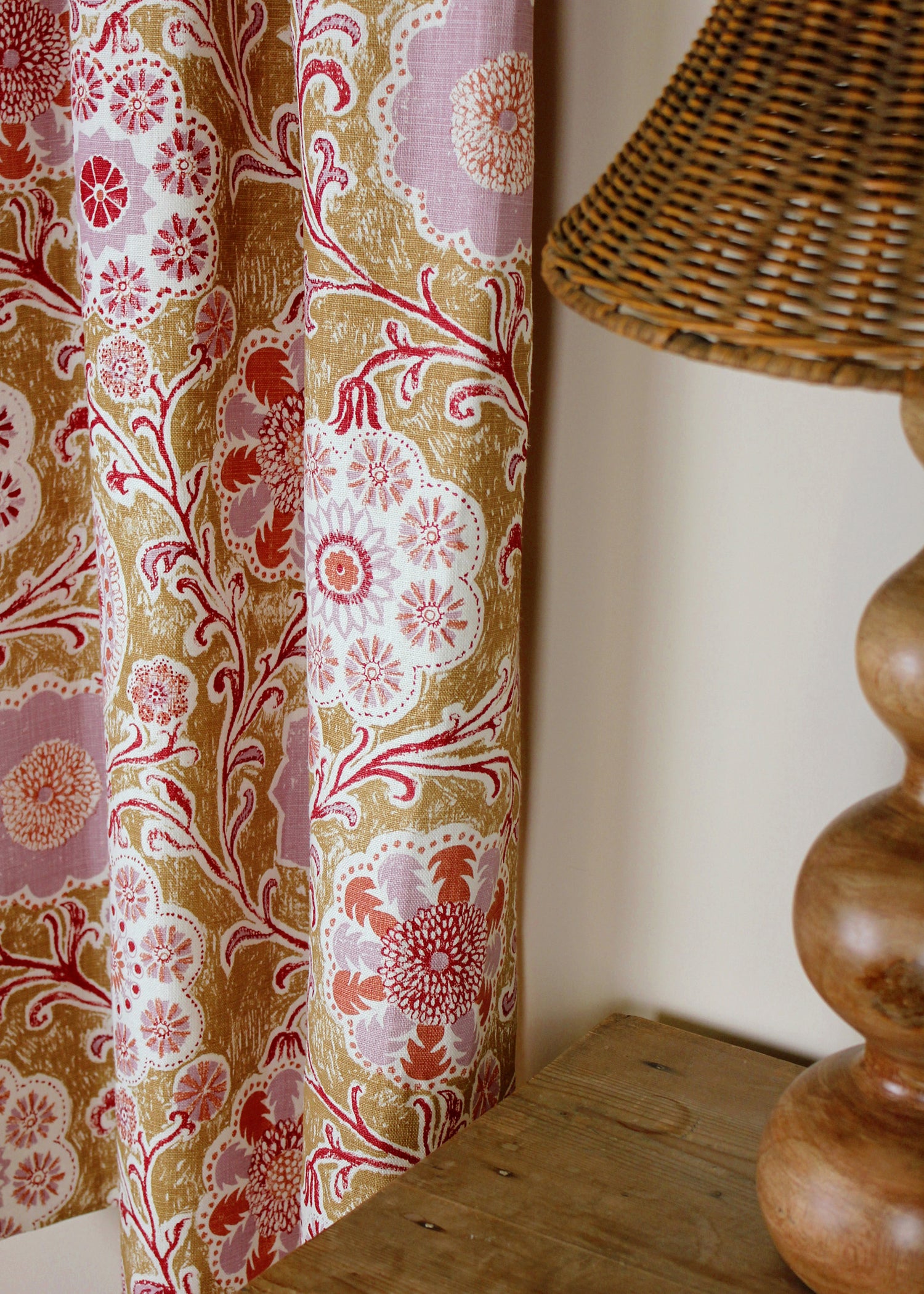 Curtain in printed linen in a handdrawn playful floral design in coral, lilac and red against a tan field. 
