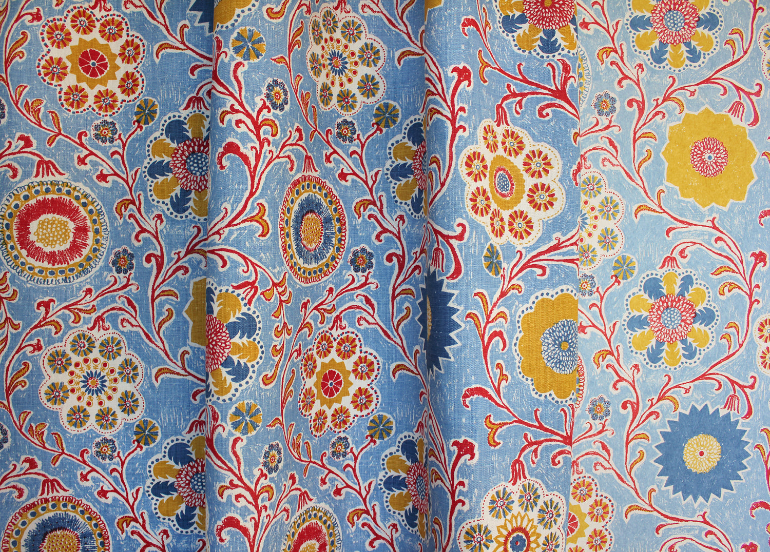 Draped printed linen in a handdrawn playful floral design in red, yellow, green and blue on a light blue field.