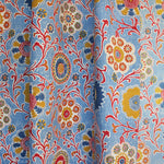 Draped printed linen in a handdrawn playful floral design in red, yellow, green and blue on a light blue field.