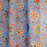 Draped printed linen in a handdrawn playful floral design in red, yellow, green and blue on a light blue field.