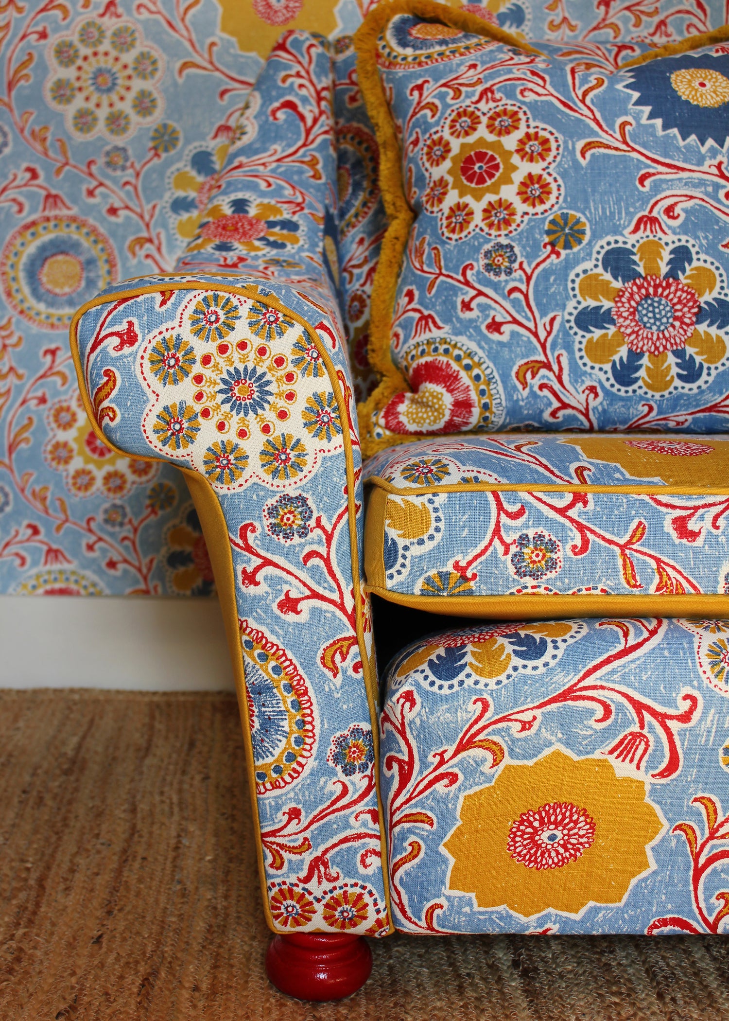 Chair upholstered in printed linen in a handdrawn playful floral design in red, yellow, green and blue on a light blue field against matching wallpaper.