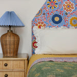 Bedroom tableau with headboard upholstered in printed linen in a handdrawn playful floral design in red, yellow, green and blue on a light blue field.