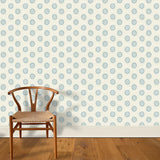 A wooden chair stands in front of a wall papered in a playful repeating floral print in blue on a cream field.