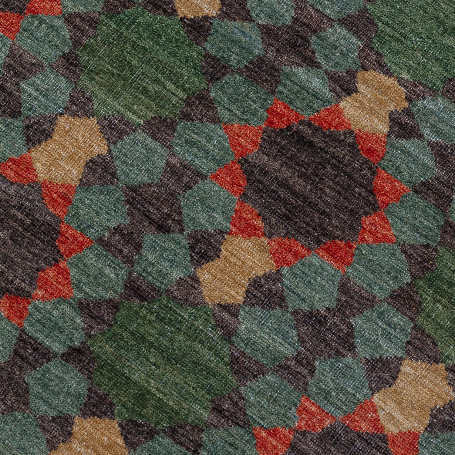 Detail of a handknotted rug in a sunburst mosaic style pattern in teal, green, red and tan. 