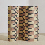 A curved partition stands on the ground, covered in a repeating triangle print in black, brown and gold.