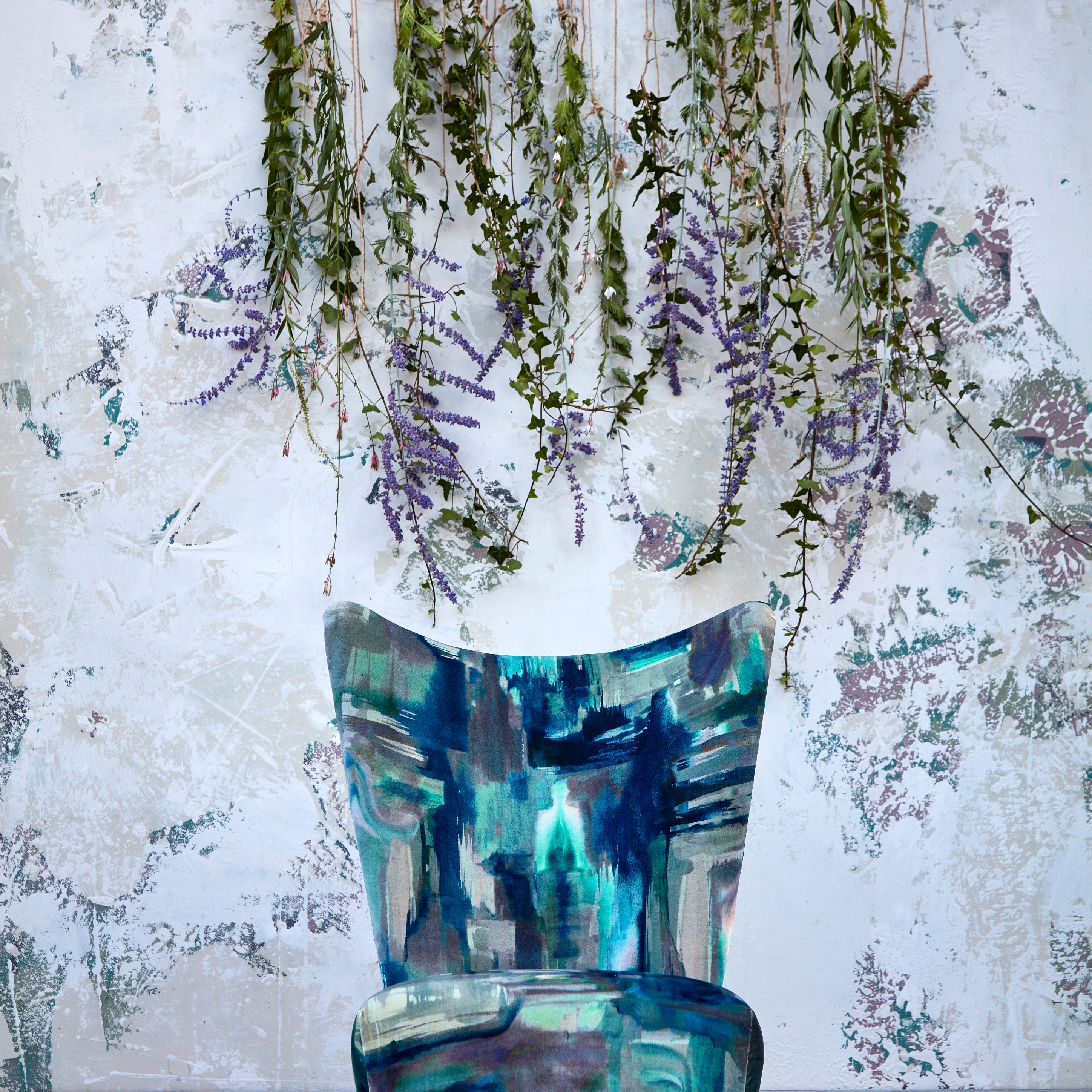 A branch covered in flowers hangs behind an armchair upholstered in a painterly print in blue and turquoise.