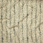Close up of gently draped printed linen with small scale painterly animal print in dark green and tan on a beige background