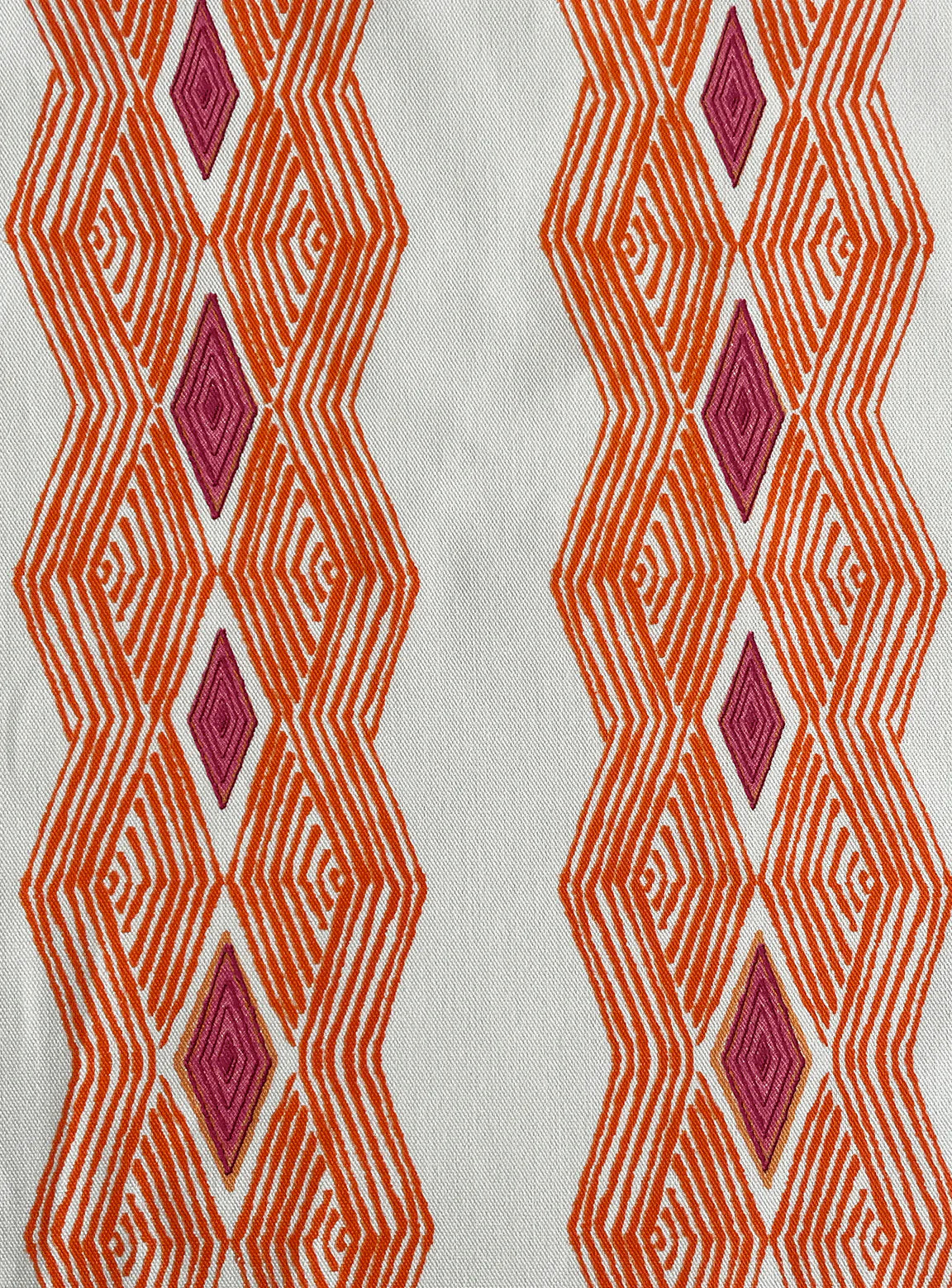 Detail of fabric in an intricate diamond stripe print in orange and pink on a cream field.
