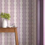 Interior with purple geometric wallpaper and matching trim with a wooden console table with white ceramic vases with flowers. 