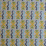 Close up of a printed fabric with blue squiggles, yellow striped triangles,  yellow X marks on a broken grid in green on a white background. 