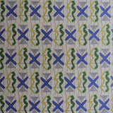 Close up printed fabric with green squiggles, white striped triangles, blue X marks on a broken grid in orange on a white background. 