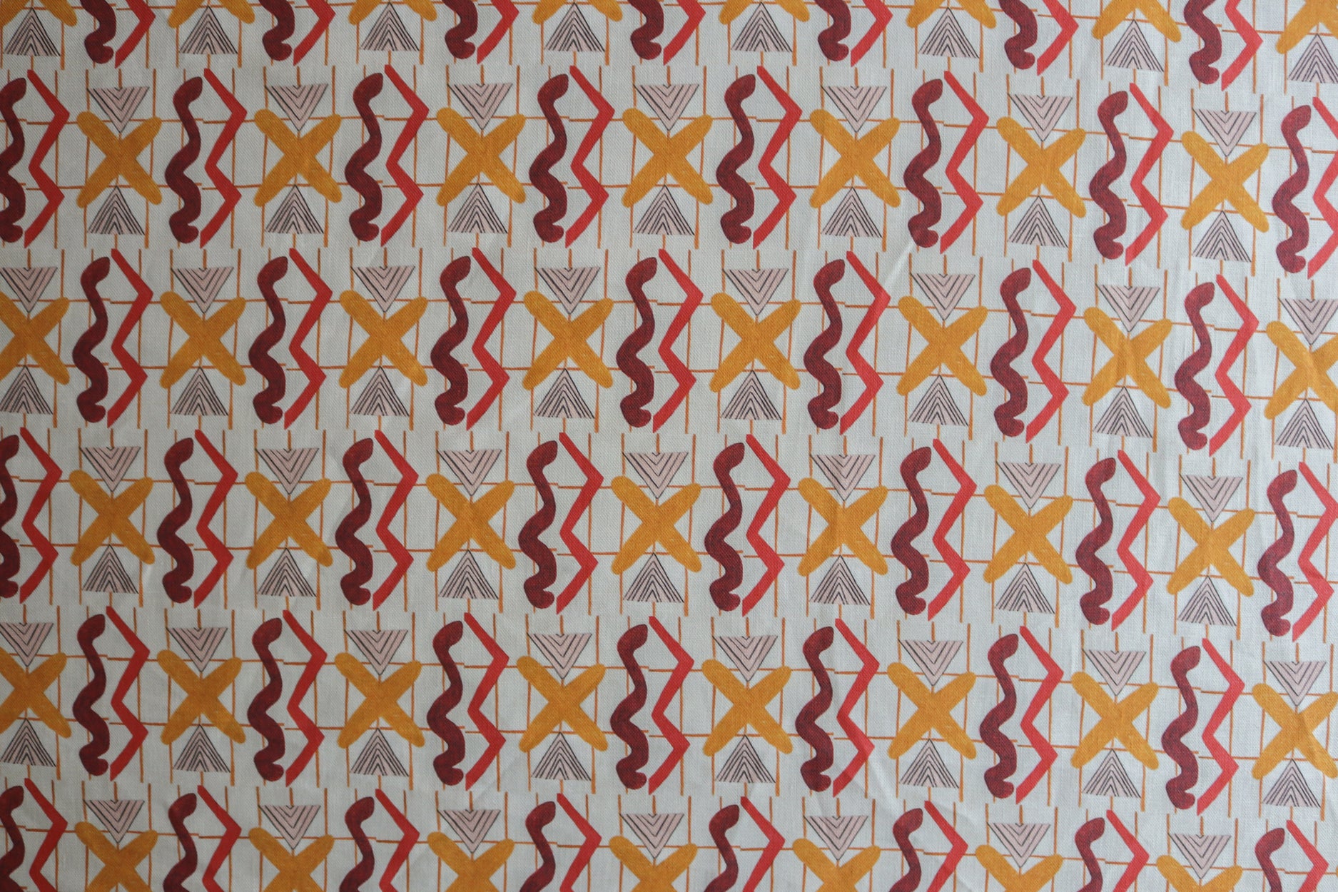 Close up of printed fabric with red squiggles, pink striped triangles, orange  X marks on a broken grid in orange on a white background. 