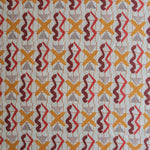 Close up of printed fabric with red squiggles, pink striped triangles, orange  X marks on a broken grid in orange on a white background. 