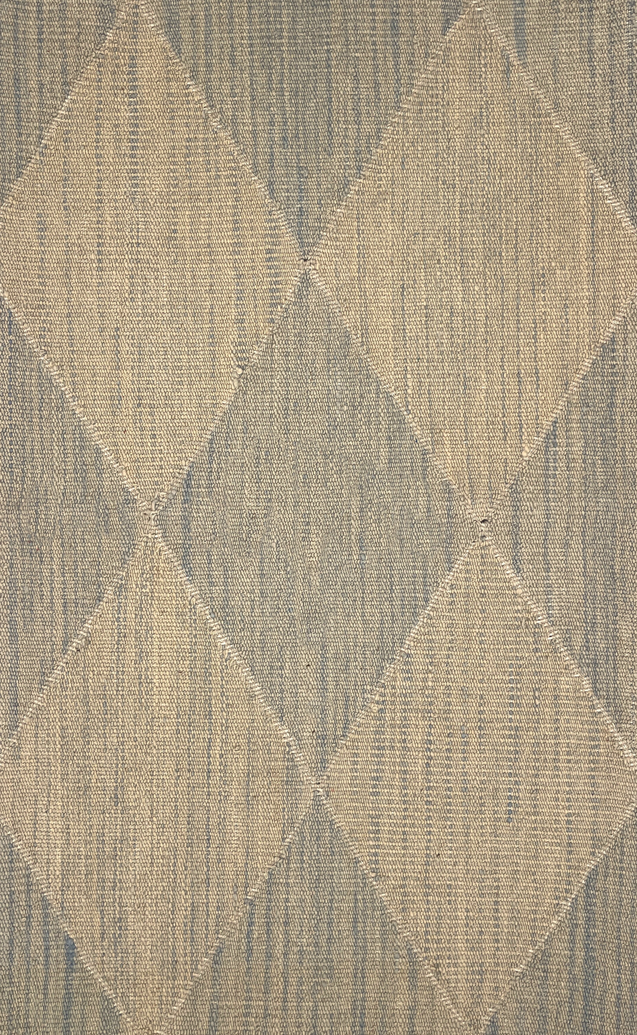 A close-up of a handwoven rug pattern featuring a diamond argyle design in beige and muted gray-blue tones.