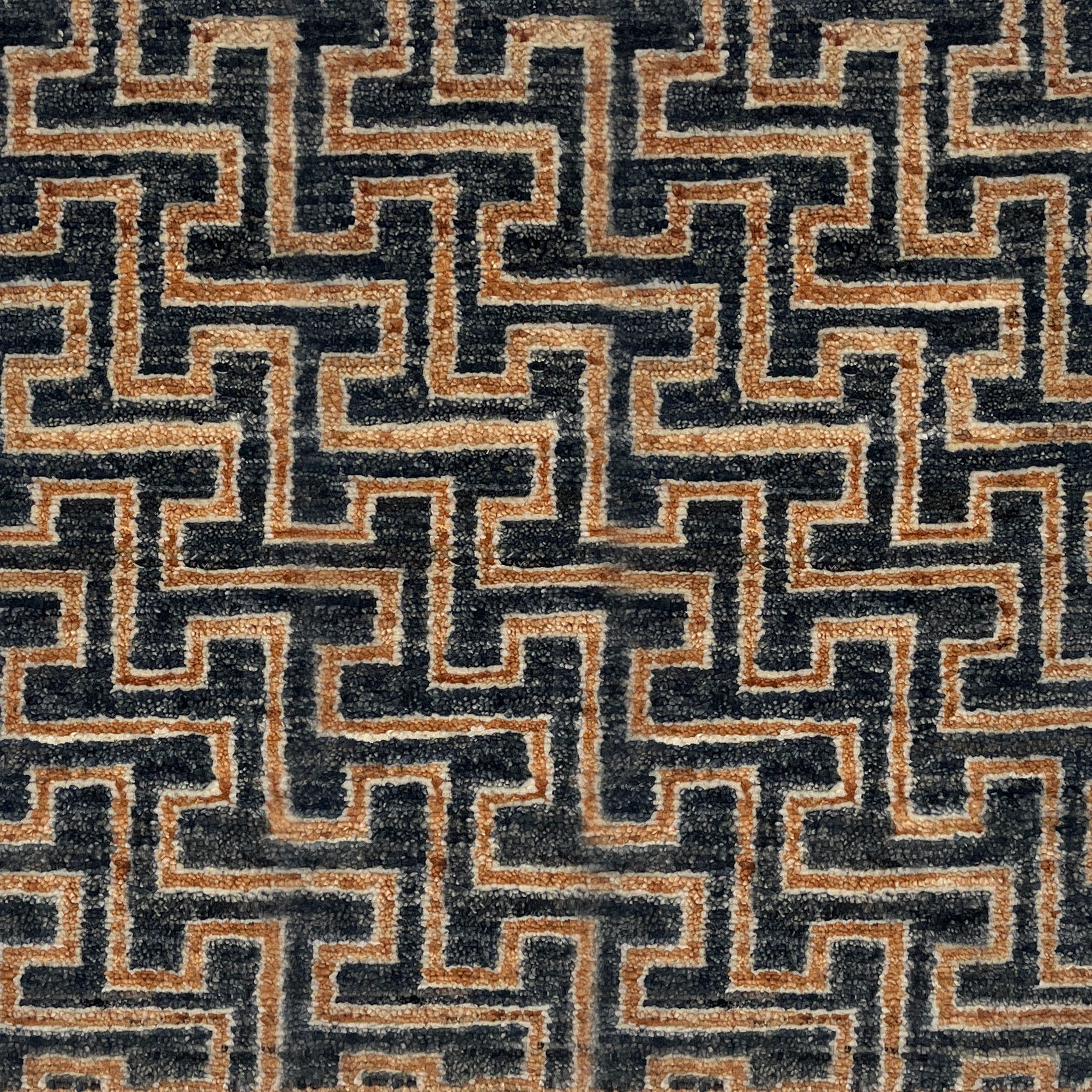 A close-up of a handknotted rug with a repeating geometric maze-like pattern in dark charcoal gray and warm tan