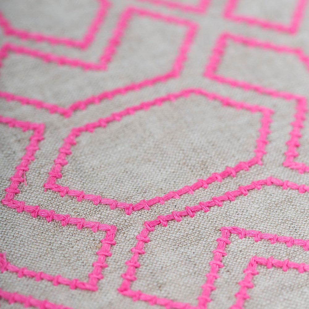 Detail of fabric with an embroidered geometric grid print in pink on a gray field.