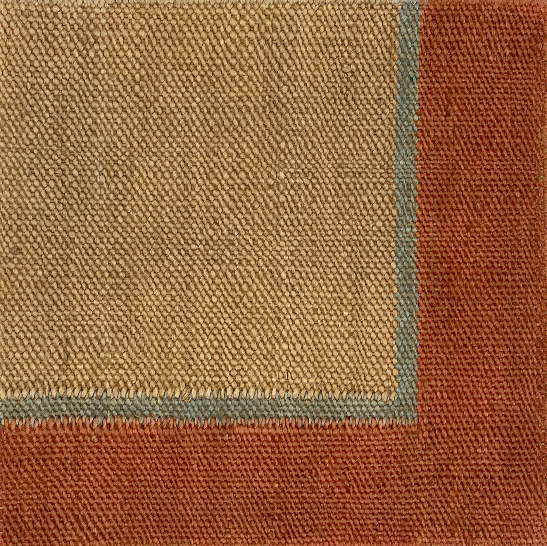 Close up of a flatweave rug in tan with a blue and coral border. 