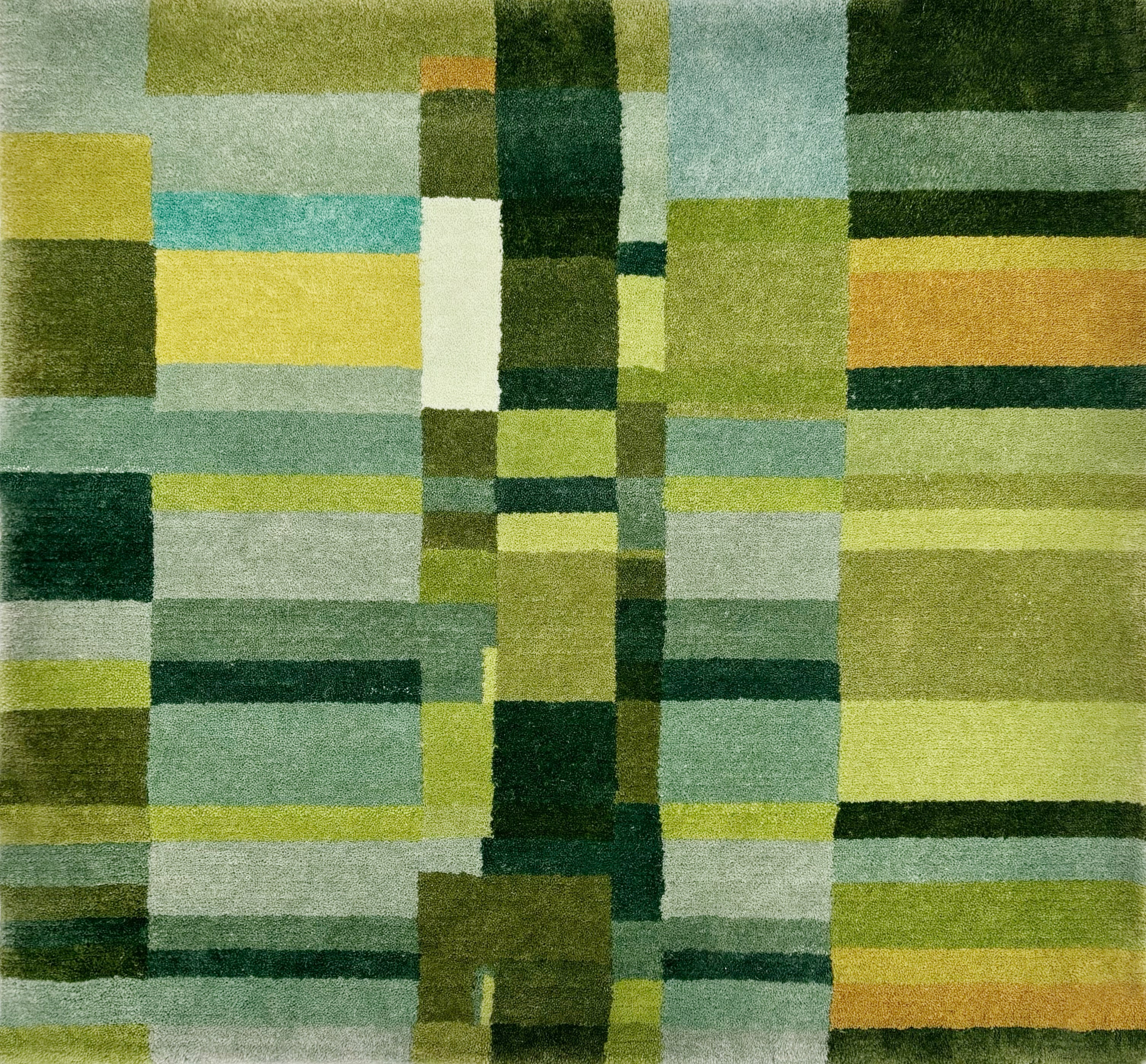 Detail of a handknotted rug in a dense geometric design in shades of a green and accents of yellow