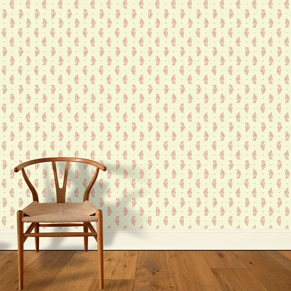 A wooden chair stands in front of a wall papered in a floral paisley print in red on a light yellow field.
