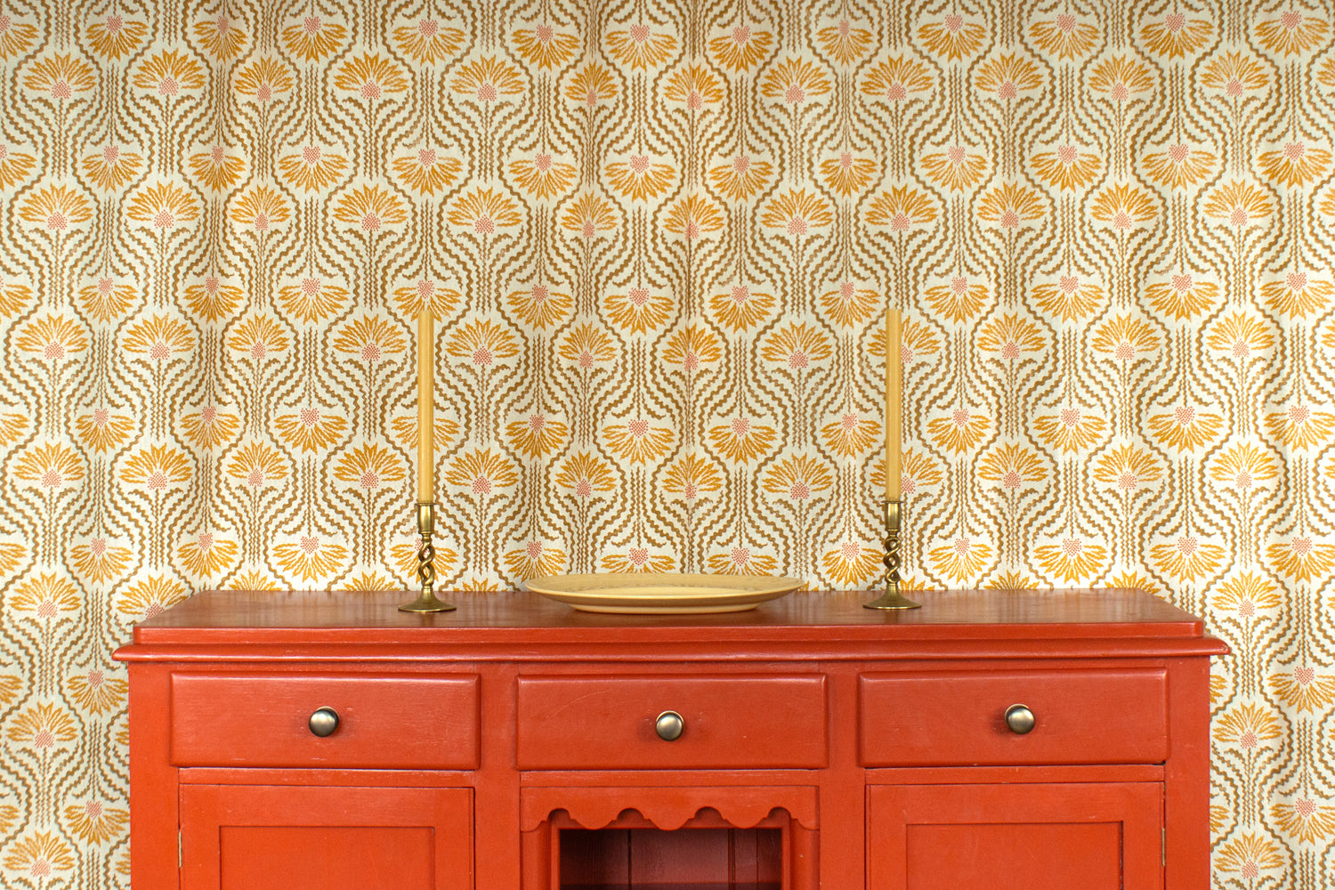 Curtain in playful yellow floral linen with an orange wooden credenza with taper candles and ceramic plate. 