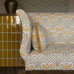 Settee upholstered in a yellow, tan and cream pattern on a dute carpet against yellow tiles. 