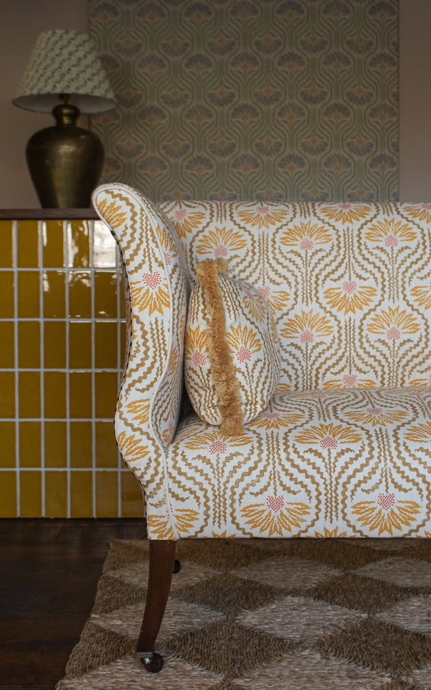 Settee upholstered in a yellow, tan and cream pattern on a dute carpet against yellow tiles. 