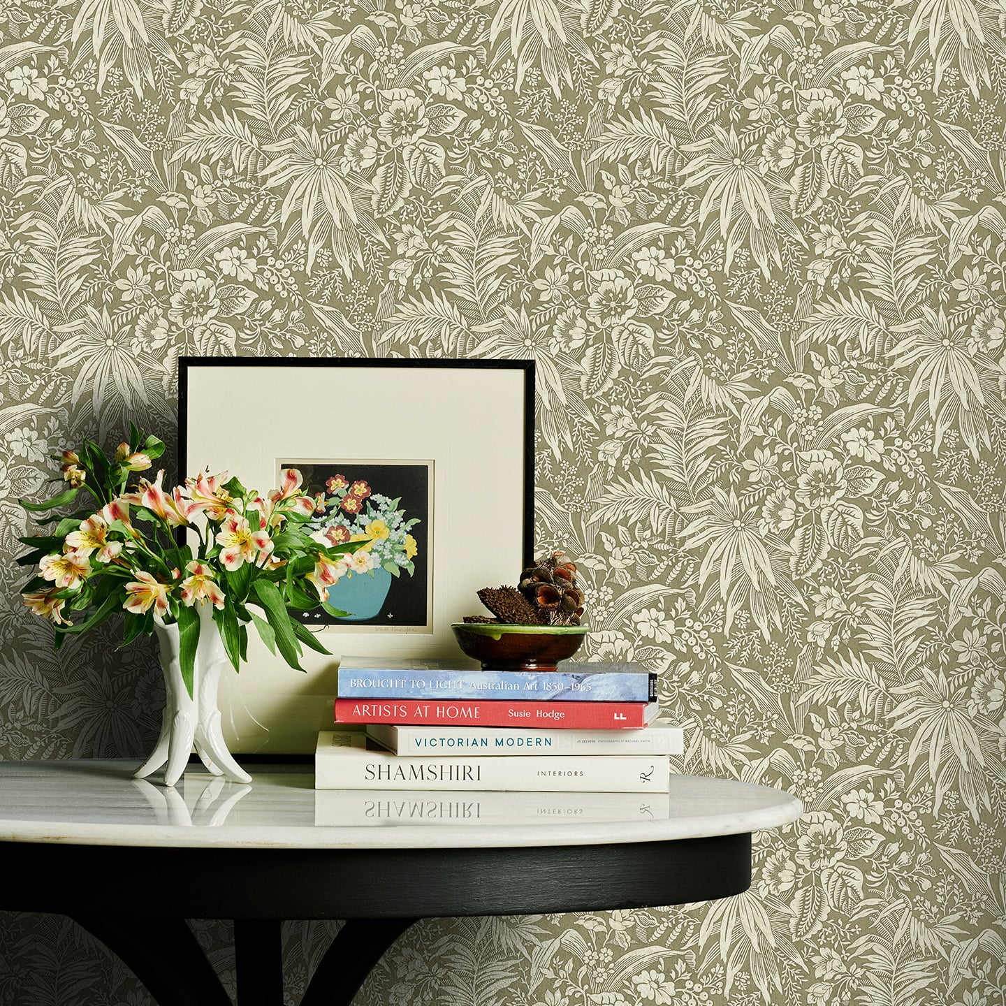 Decorative table with books and flowers against a green floral wallpapered wall.
