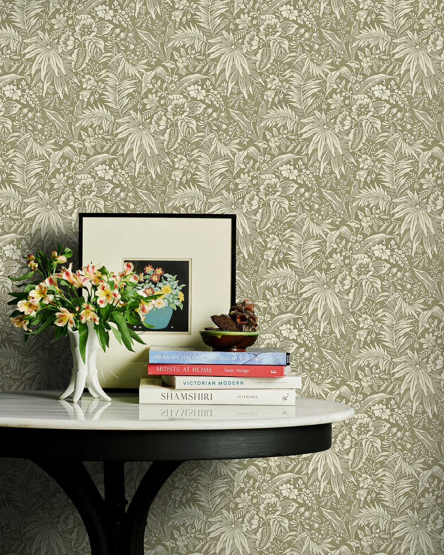 Decorative table with books and flowers against a green floral wallpapered wall.