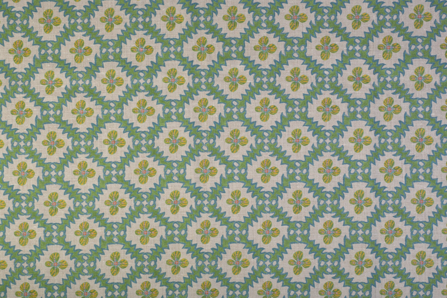 Detail of fabric in a playful floral grid print in green, yellow and blue on a white field.
