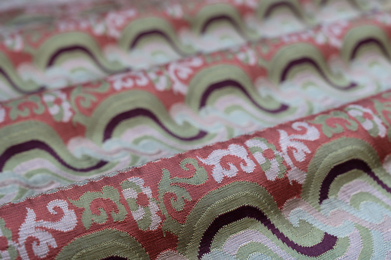 Close-up of folded handwoven silk fabric with a wavy pattern in red, green, and white.