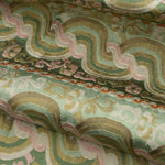 Close-up of folded handwoven silk fabric with wavy patterns in green, pink, and tan.