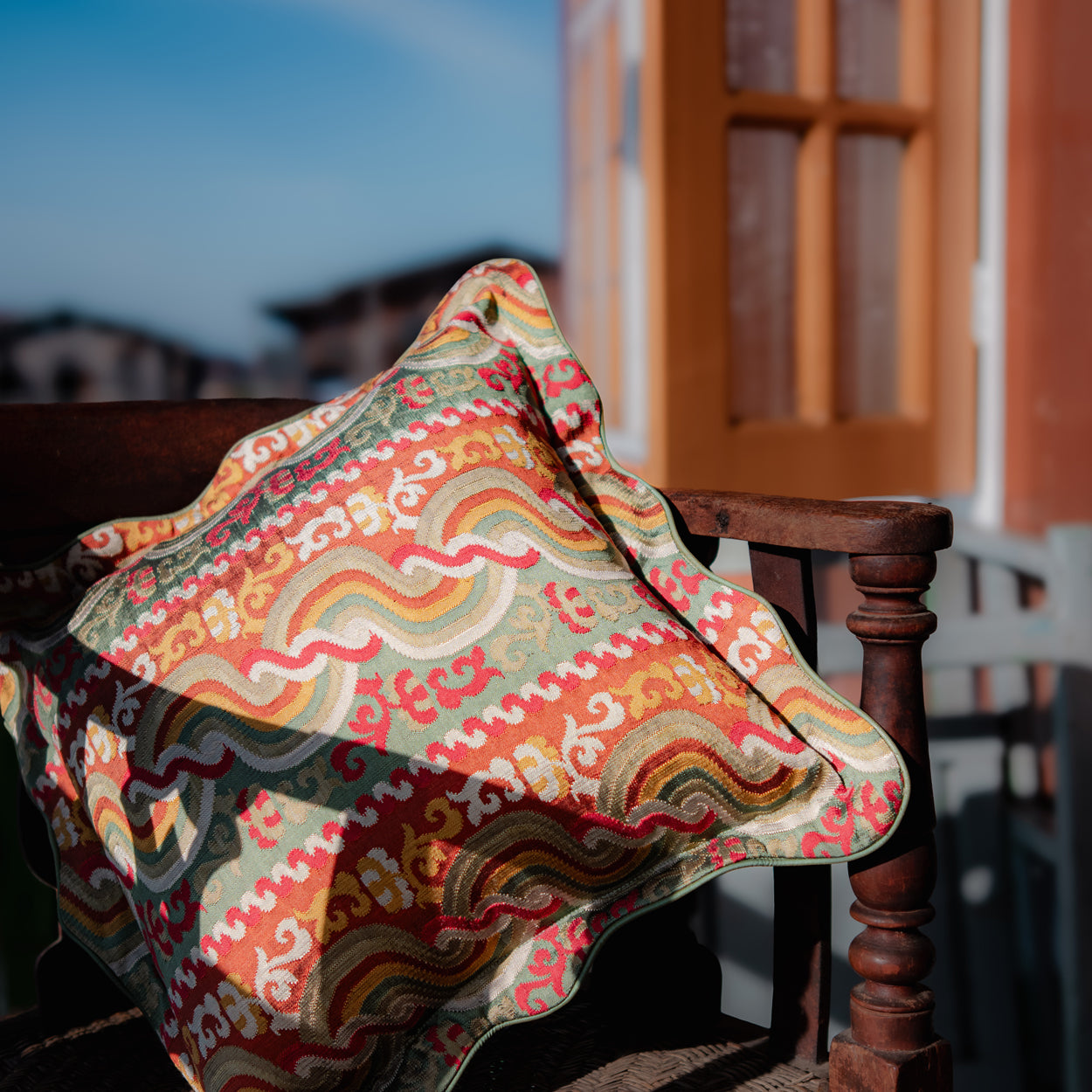 Colorful patterned fabric pillow on a wooden chair with a blurred outdoor setting