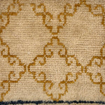 Handknotted rug sample with an ochre filigree design on a beige field.