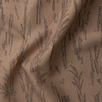 Detail of gently draped printed fabric with a black pointillist wheat frond pattern on a warm brown background. 