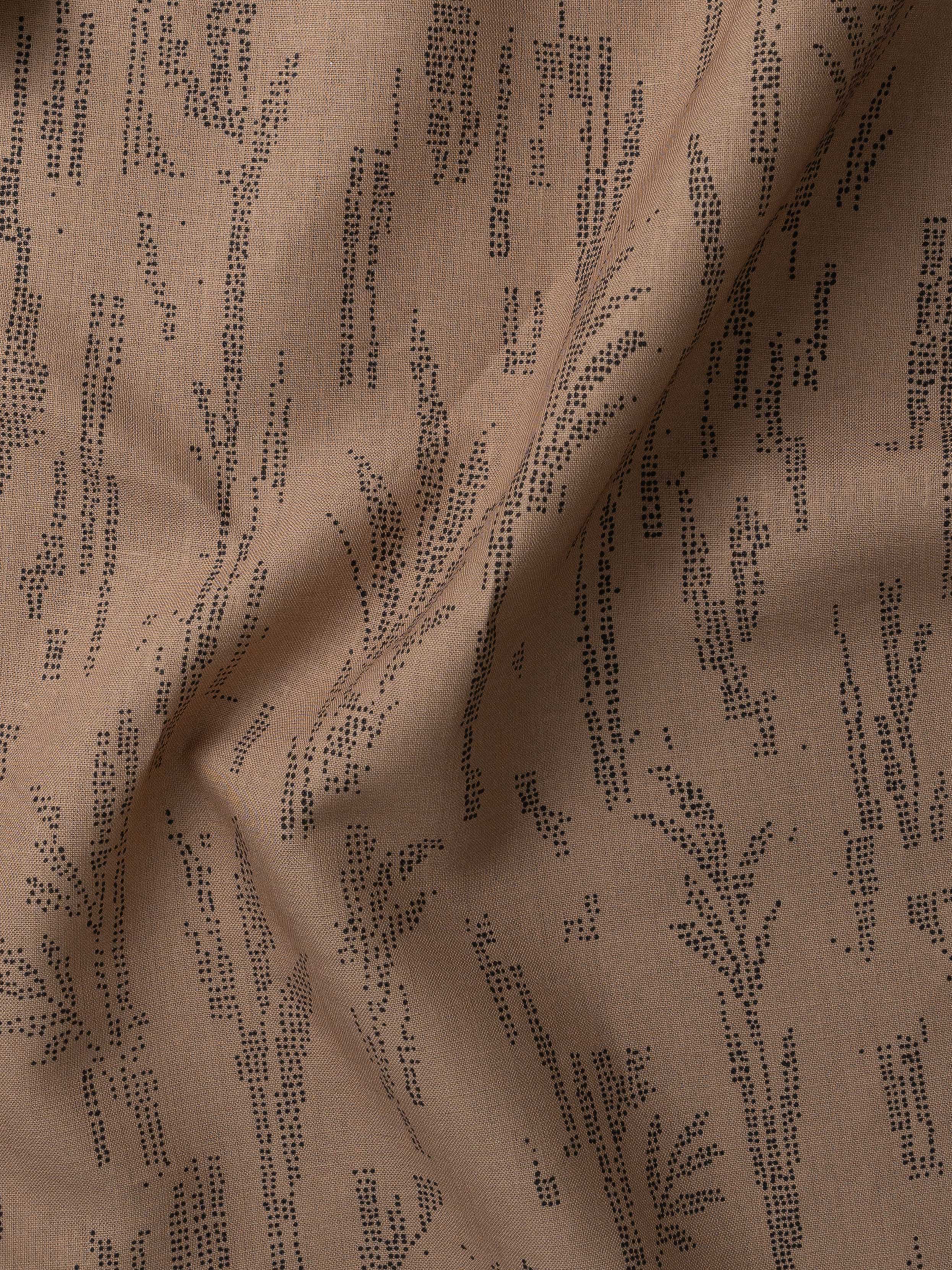 Detail of gently draped printed fabric with a black pointillist wheat frond pattern on a warm brown background. 