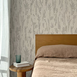 Bed with tan linens and wooden headboard, wooden side table  with white book and green glass, white floor length curtain against a black pointillist wheat frond patterned wallpaper on an ecru background. 