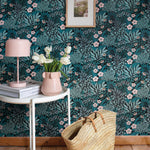 An end table and basket stand in front of a wall papered in a dense floral print in turquoise, pink and black.