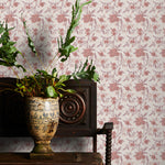 Decorative plant in a vase on a wooden table with pink floral wallpaper in the background