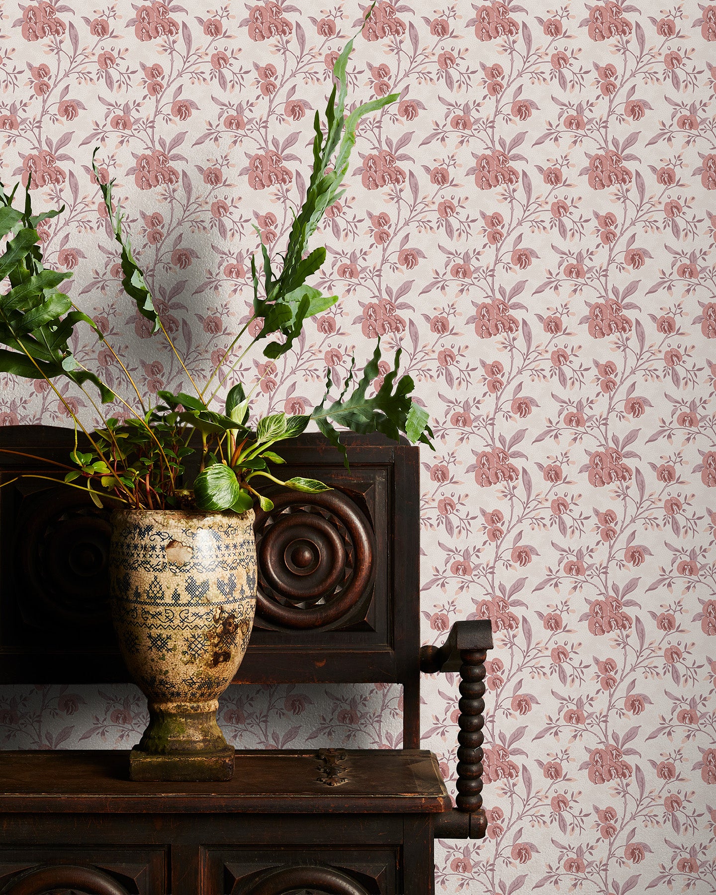 Decorative plant in a vase on a wooden table with pink floral wallpaper in the background