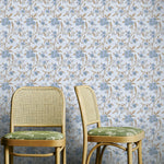 Two wicker chairs with green cushions against a blue and brown floral wallpapered wall.